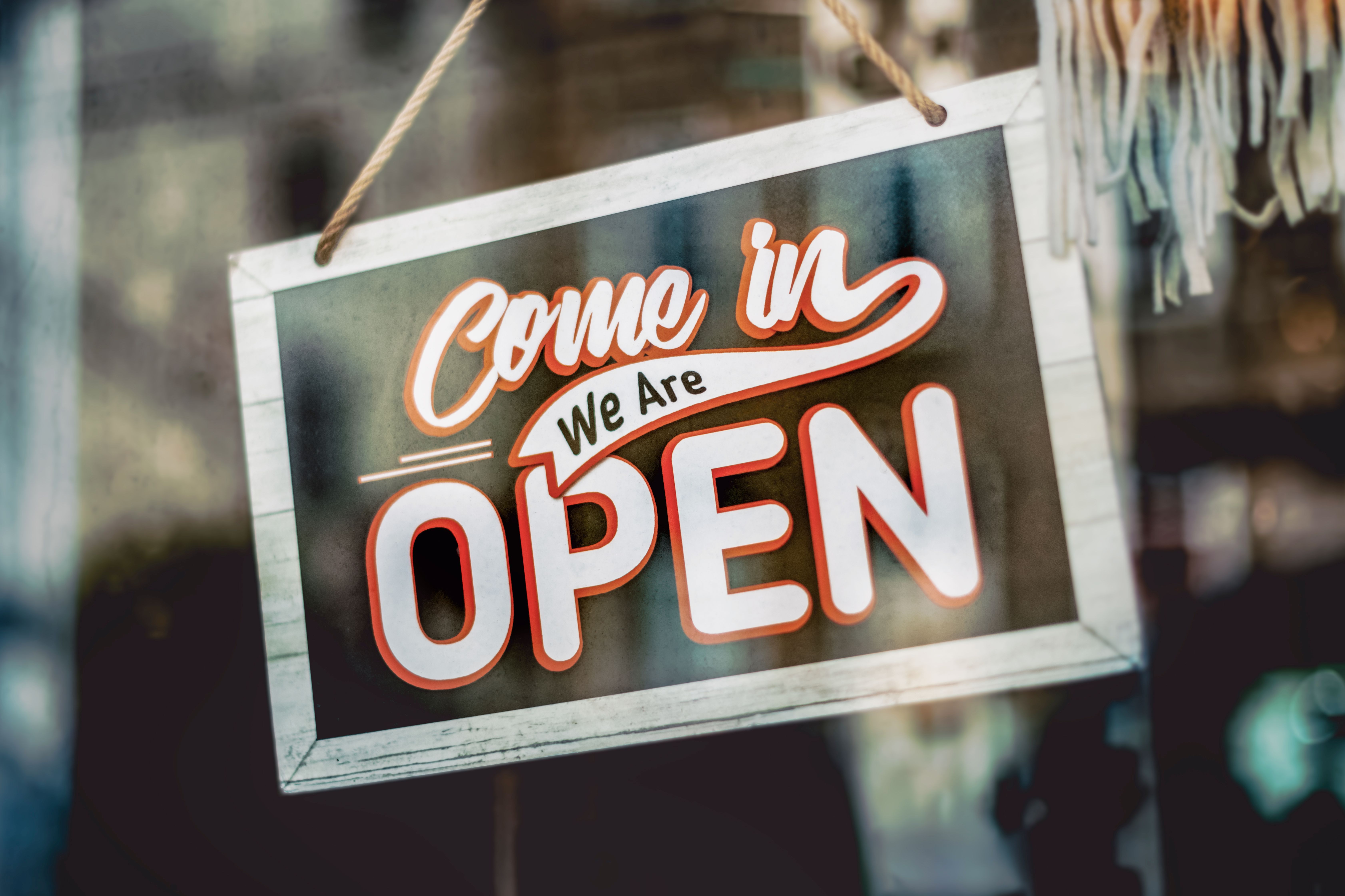 'Come in, We Are Open' sign hanging on the glass window of a shop